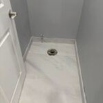 Bathroom remodel in progress showing newly tiled floor and plumbing ready for toilet installation.