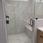 Spacious walk-in shower with frameless glass, large white tiles, and rainfall showerhead.