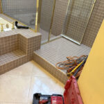 Outdated tiled shower and bathtub combo with gold trim and brown square tiles before renovation.