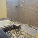 Demolition in progress of vintage tiled bathroom with debris from removed bathtub and shower walls.