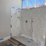 Freestanding bathtub filler installed near new tile shower during bathroom remodel with floor protection in place.